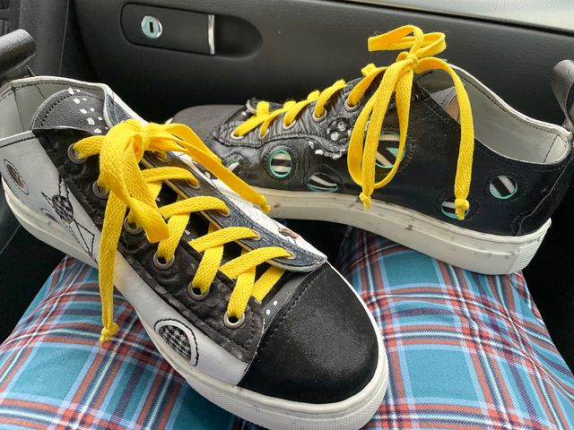 Erin's low-top shoes on my lap --
mostly flat black-and-white,
with cutout circles revealing black-and-white patterns beneath.
They have black toe caps, bright yellow laces,
and angular black stitching across the circles.
