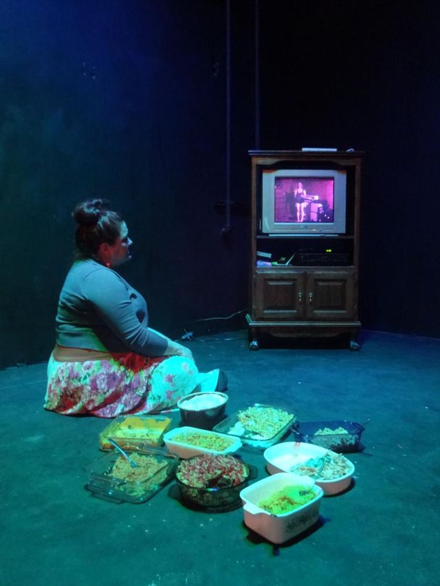 Jenny watching Sam undress on an old TV, surrounded by casseroles