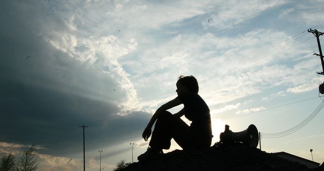 Silhouette sitting on a hill, beside a bullhorn