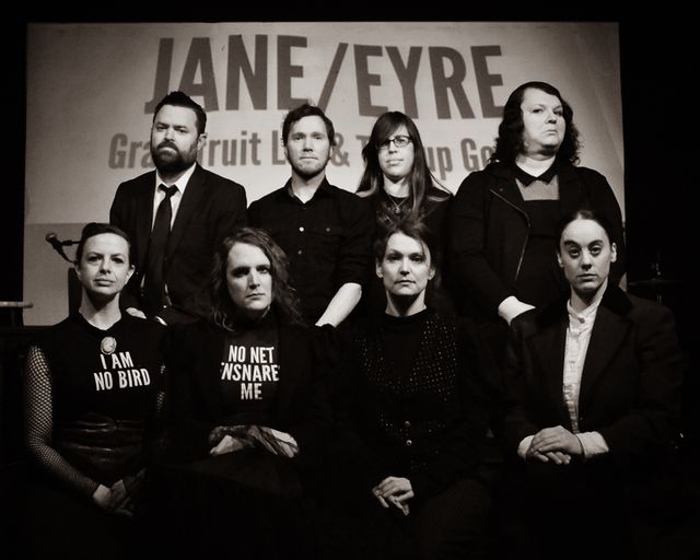 The entire ensemble looking sternly at the camera,
in black and white.
Dameon, Dan, Sondra, and Josie across the back,
with Lindsey, Miriam, Julue, and Meghan in front.
Lindsey's shirt says I am no bird.
Miriam's says No net ensnares me.
The projection behind them says
Jane/Eyre, Grapefruit Lab & Teacup Gorilla.
