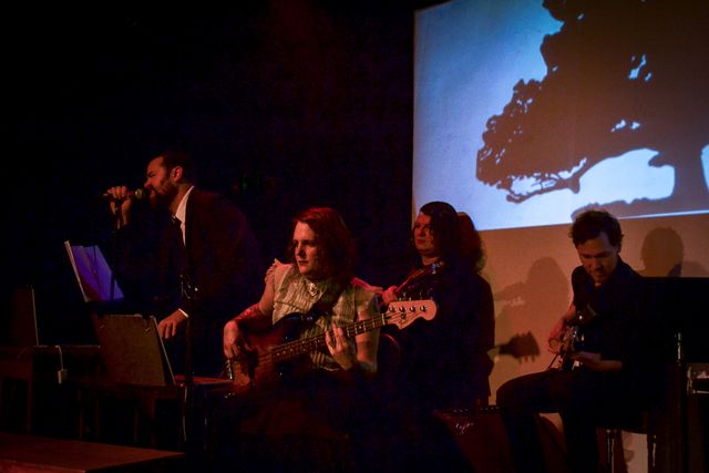 Miriam as narrator Jane on bass,
Dan and Josie on guitar,
and Dameon singing.
Behind them, the silhouette of a tree.
