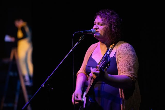 Josie singing in the foreground,
with Miriam on a ladder out of focus behind her
