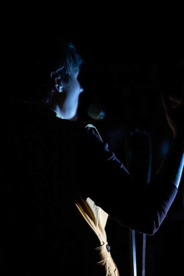 Miriam from behind at a microphone,
mostly dark, but glowing with a blue light on her face
