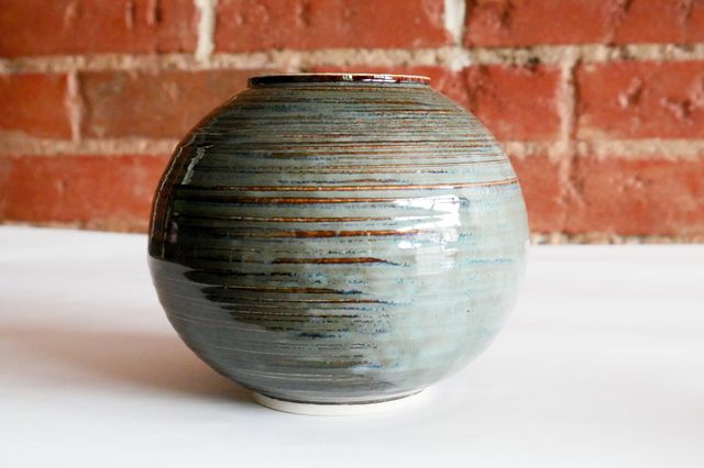 A nearly-spherical vase with a small protruding foot ring and lip, and textured grooves highlighted by the green-gray glaze that breaks red-brown over the texture.