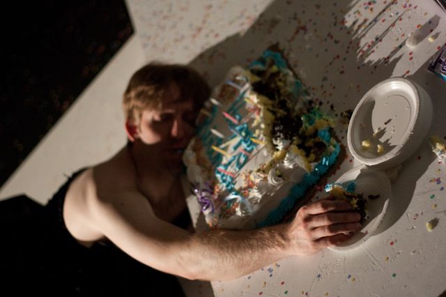 Matt Shultz in a black dress, splayed face-down in a birthday cake